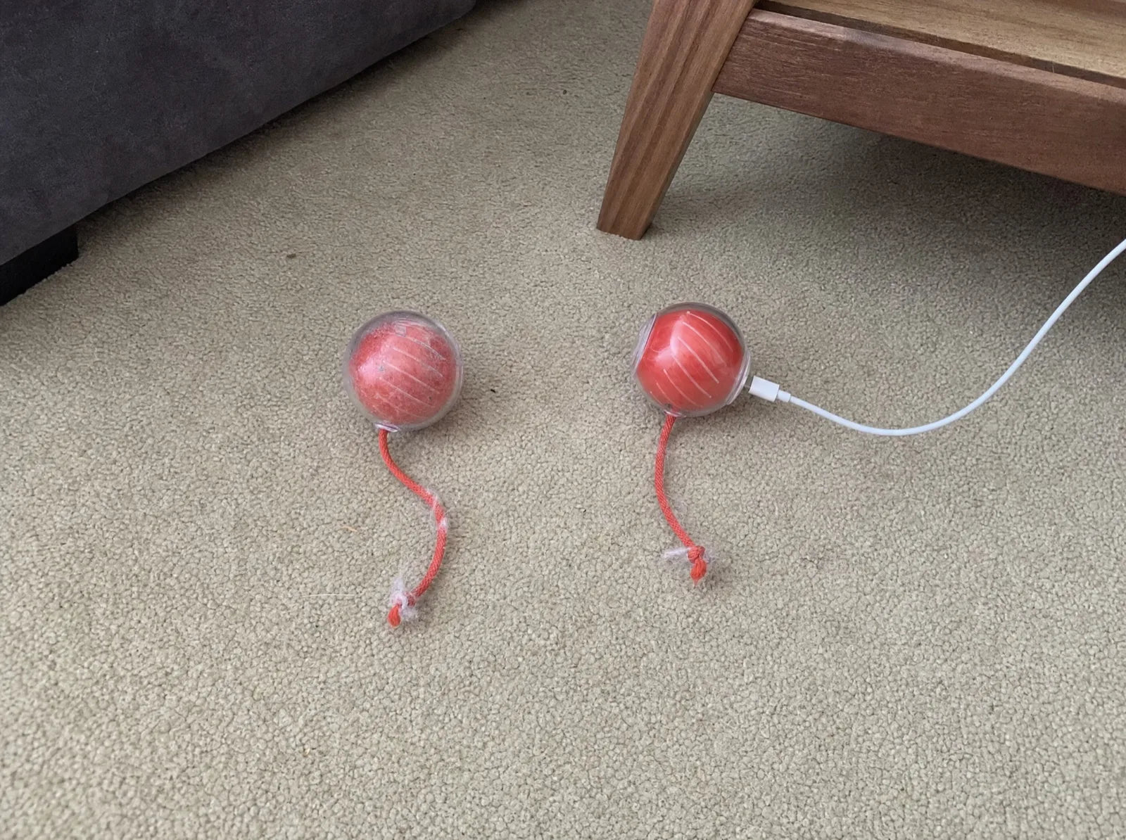 Two cheap red smart balls stalled on the carpet, one still on charge
